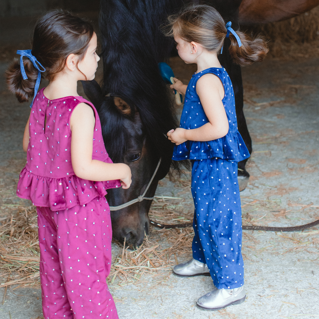 Two little rockstars in Piglo Kids playful sequine velvet sets, one in red and one in blue, interacting with a horse in a stable